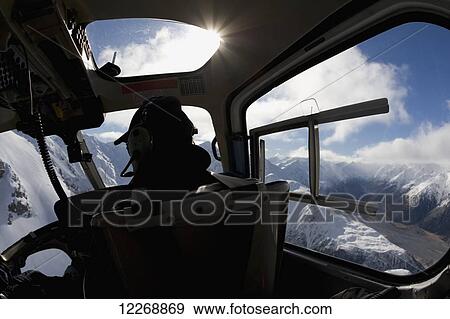 Stock Photo - View of helicopter pilot in a cockpit looking out over the snowy mountain tops; New Zealand. Fotosearch