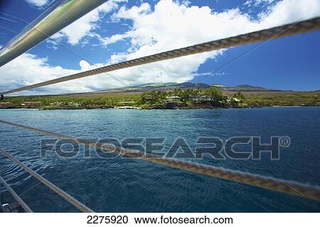 Stock Image - View of the coastline of an hawaiian island through the railing of a boat; Hawaii, United States of America. Fotosearch