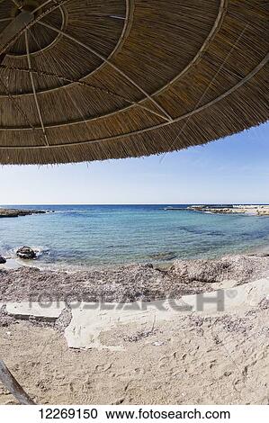 Stock Image - View of the mediterranean from under a thatched umbrella at the water's edge; Paphos, Cyrpus. Fotosearch