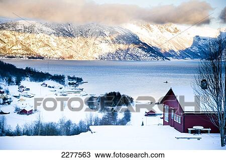 Stock Image - View of the village, Fjord and mountains with the sun setting over the mountains; Ortnevik, Sognefjord, Norway. Fotosearch