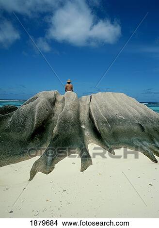 Picture - View Of Woman From Back Sitting On Rocks At The Beach. Fotosearch