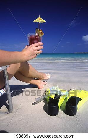 Stock Photo - View Of Woman's Legs And Hand Holding Drink On Beach, In Beachchair With Snorkel Gear.. Fotosearch