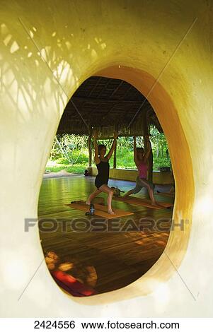 Stock Photograph - View through a round window of women doing yoga; Ulpotha, Embogama, Sri Lanka. Fotosearch