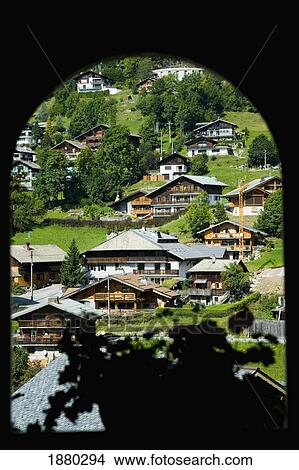 Picture - View Through Arched Window Of Alpine Lodges And Chalets On Hillside. Fotosearch