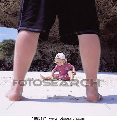 Stock Image - View Through Father's Legs Of Child Playing In Sand. Fotosearch