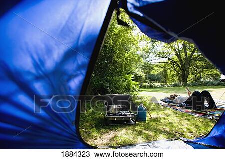 Stock Image - View Through Tent Of Campsite And Woman Reading. Fotosearch