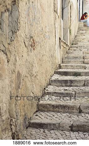 Stock Photograph - View Up Old Steps To A Woman Sitting In A Doorway In Alfama.. Fotosearch
