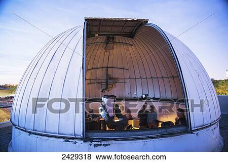 Stock Photo - Visitors look through a telescope in an observatory at York University; Toronto, Ontario, Canada. Fotosearch