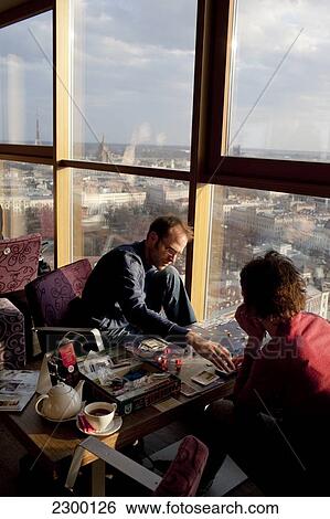Stock Photograph - Visitors play a board game on the 26th floor of the Reval Hotel Skyline Bar, at sunset, Riga, Latvia.. Fotosearch