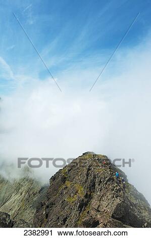 Stock Image - Walkers going along ridge above clouds in the Black Cuillin; Isle of Skye, Scotland. Fotosearch