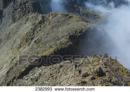 Stock Image - Walkers going along ridge above clouds in the Black Cuillin; Isle of Skye, Scotland. Fotosearch