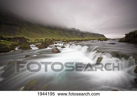 Stock Photography - Water Cascading Over Rock In A River Under A Cloudy Sky; Iceland. Fotosearch