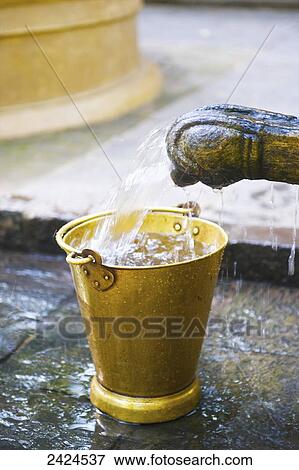 Stock Photo - Water pouring into a small yellow bucket from a tap; Ulpotha, Embogama, Sri Lanka. Fotosearch