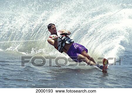 Stock Image - Water Skier In Turn Causing Spray Close-Up Man Holding On Diagonal Ocean. Fotosearch
