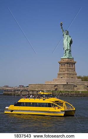 Stock Image - Water Taxi Passing Statue Of Liberty In Lower Manhattan; New York City, Usa. Fotosearch