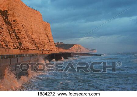 Stock Image - Waves Crashing Against Wall By Walkway And Cliffs. Fotosearch