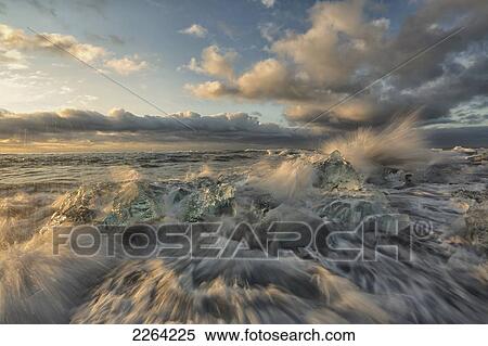 Stock Photography - Waves from the atlantic ocean crashes over icebergs along the coast at sunrise; iceland. Fotosearch