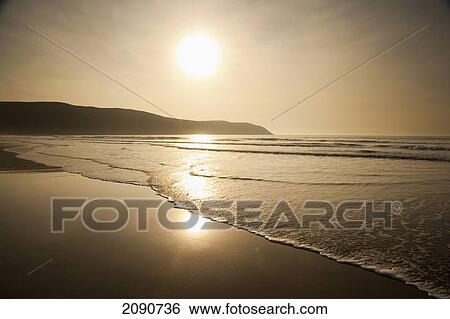 Stock Photograph - Waves Lapping Up On The Shore At Sunset At Putsborough Sands, North Devon, Uk. Fotosearch