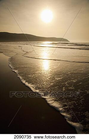 Waves Lapping Up On The Shore At Sunset At Putsborough Sands, North Devon, Uk View Large Photo Image Stock Photography - Waves Lapping Up On The Shore At Sunset At Putsborough Sands, North Devon, Uk. Fotosearch