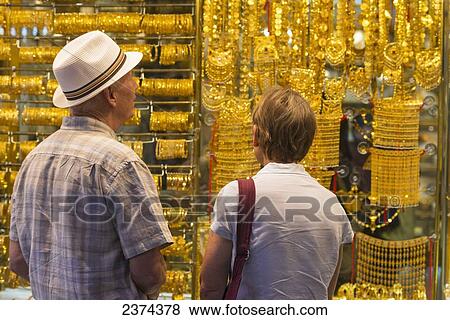 Stock Photo - Western couple looking at gold jewellery for sale in window of shop in the gold souk; Dubai, United Arab Emirates. Fotosearch