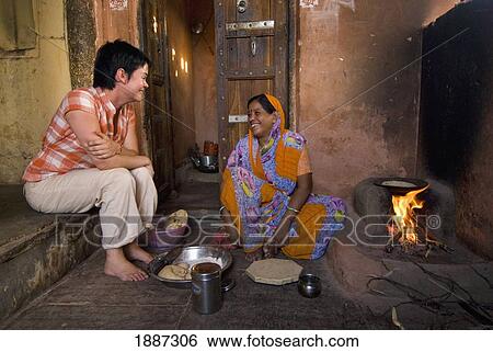 Stock Photograph - Western Woman Chatting With Indian Lady As She Cooks Chapatis And Prepares Meal. Fotosearch