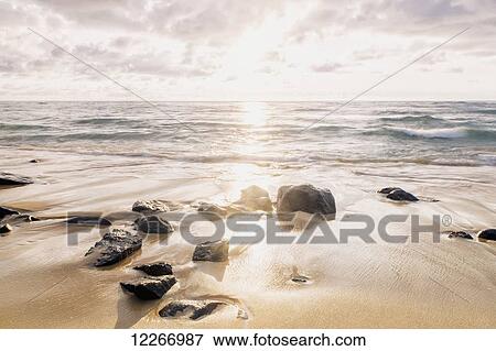 Stock Photo - Wet sand and rocks on the beach after sunrise; Wailua, Kauai, Hawaii, United States of America. Fotosearch