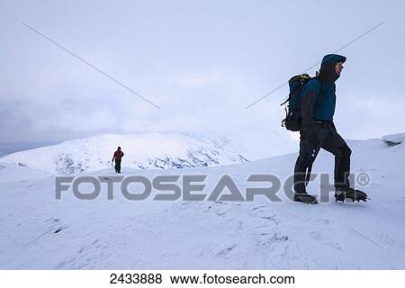 Stock Photo - Woman and man walking up Beinn Dorain in snowy, winter conditions, near Bridge of Orchy; Argyll and Bute, Scotland. Fotosearch