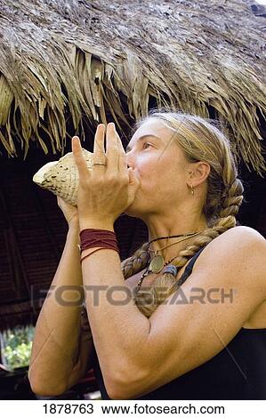 Stock Image - Woman Blowing Through A Conch Shell. Fotosearch
