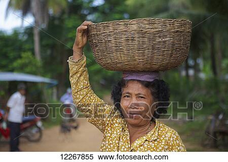 Stock Photography - Woman carrying a basket on her head; Battambang, Cambodia. Fotosearch