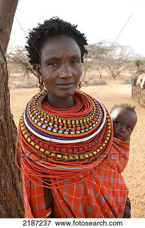 Stock Photo - Woman carrying baby in sling wearing colourful beaded necklace, Sumburu Manyatta village; Samburu, Kenya. Fotosearch