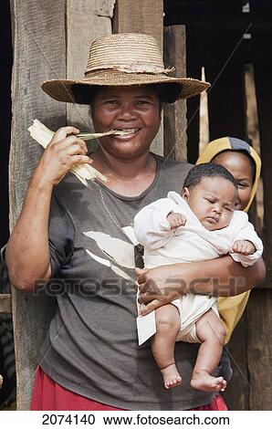 Stock Image - Woman Chewing On A Piece Of Sugar Cane, As She Is Holding Her Baby, Ambalavao, Fianarantsoa Province, Madagascar. Fotosearch