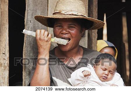 Stock Photo - Woman Chewing On A Piece Of Sugar Cane, As She Is Holding Her Baby, Ambalavao, Fianarantsoa Province, Madagascar. Fotosearch