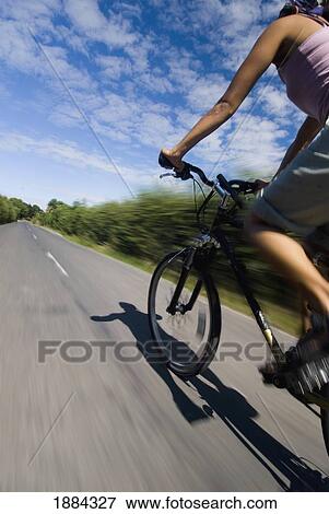 Stock Photo - Woman Cycling Down Small Country Road. Fotosearch
