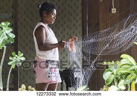 Stock Image - Woman fixing a fishing net, Pulao Asei, island in Lake Sentani, Papua, Indonesia. Fotosearch