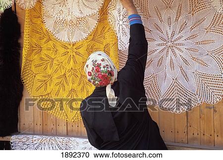 Stock Image - Woman Hanging Traditional Lace Tablecloths In Street Market. Fotosearch