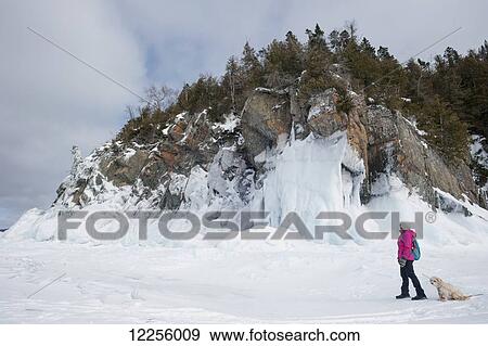 Woman hiking in winter on a frozen lake near an icy rocky shore with her pet dog; Ontario, Canada View Large Photo Image Stock Photo - Woman hiking in winter on a frozen lake near an icy rocky shore with her pet dog; Ontario, Canada. Fotosearch