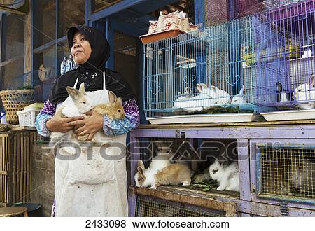 Stock Photo - Woman holding rabbits at the bird market, Yogyakarta, Java Island, Indonesia. Fotosearch