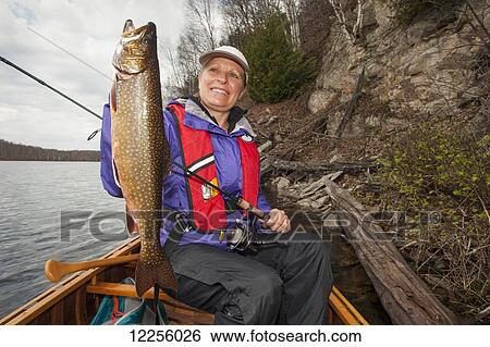 Stock Photograph - Woman holds a large splake fish in a canoe near shore on a lake; Ontario, Canada. Fotosearch