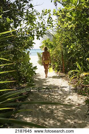 Stock Photography - Woman in bikini walking on sand trail to beach, Coco Palm Dhuni Kolhu Island; Maldives. Fotosearch