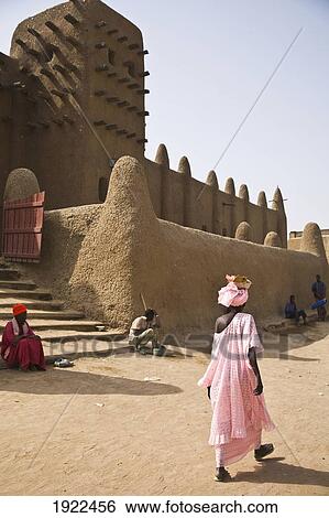 Stock Photograph - Woman In Pink Gown Walking In Front Of Djenne Mosque. Fotosearch