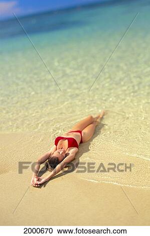 Stock Image - Woman In Red Bikini With Arms Above Head Laying In Waters Edge, Selective Focus. Fotosearch