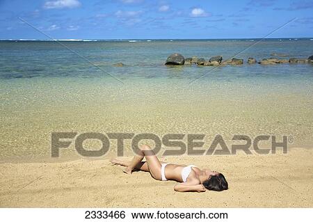 Stock Photograph - Woman in strapless white bathing suit laying out on the beach; Kauai, Hawaii, United States of America. Fotosearch