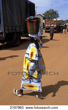 Stock Image - Woman In Traditional Dress Carrying Pot On Head, Barra Port, The Gambia. Fotosearch
