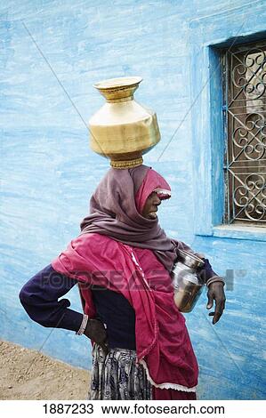 Stock Image - Woman In Traditional Dress Carrying Brass Pot On Her Head. Fotosearch