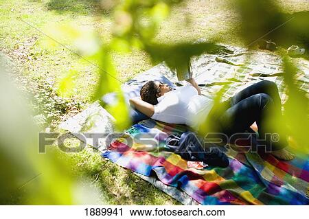 Stock Image - Woman Lying Down On Grass Reading In Woods. Fotosearch