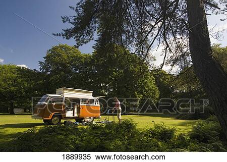 Stock Photography - Woman Making Tea Outside Old Campervan In Forest Clearing. Fotosearch