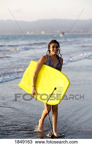 Stock Image - Woman On Beach Carrying Bodyboard. Fotosearch