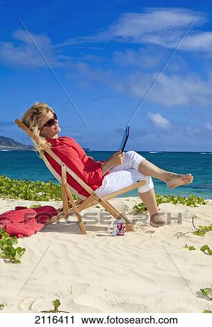 Stock Image - Woman on beach uses electronic tablet.. Fotosearch