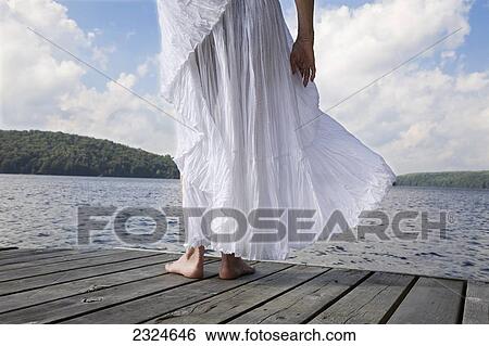 Stock Photograph - Woman On Cottage Dock With White Skirt Blowing In The Wind, Ontario, Canada. Fotosearch