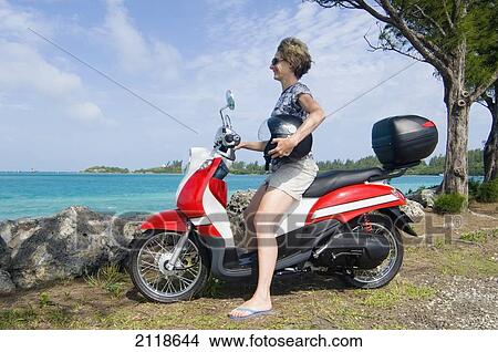 Picture - Woman On Red And White Scooter Smiling And Looking At Water; Bermuda. Fotosearch